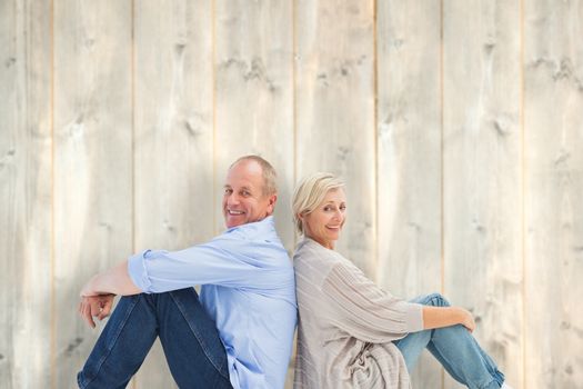 Happy mature couple smiling at camera against pale wooden planks