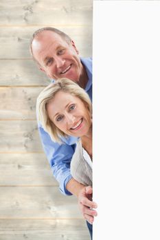 Mature couple smiling behind wall against pale wooden planks