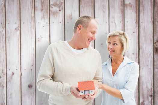 Happy mature couple with model house against wooden planks