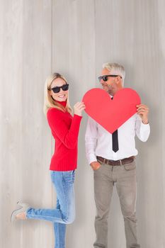 Cool couple holding a red heart together against bleached wooden planks background