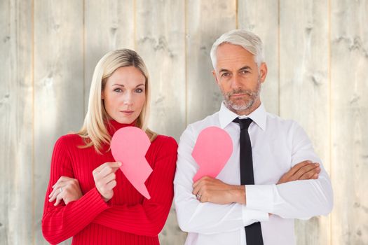 Couple not talking holding two halves of broken heart against pale wooden planks