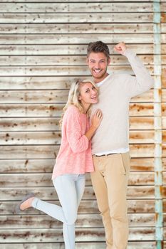 Attractive couple smiling and cheering against faded pine wooden planks