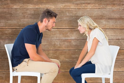 Young couple sitting in chairs arguing against wooden planks background