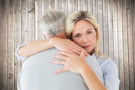 Unhappy blonde hugging her husband against wooden planks background