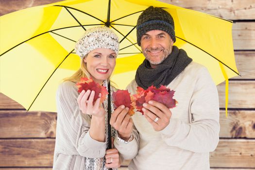 Couple in winter fashion showing autumn leaves under umbrella against wooden planks background