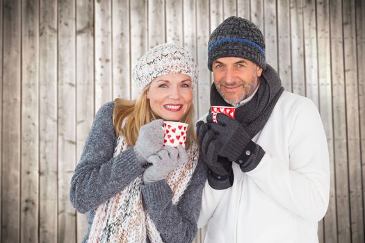Happy couple in winter fashion holding mugs against wooden planks background