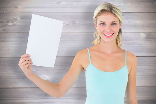 Happy blonde holding a sheet of paper against wooden planks background
