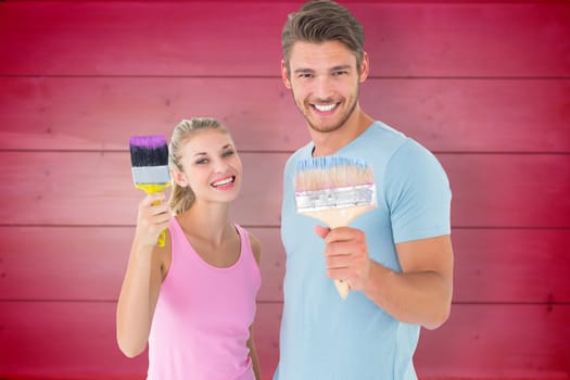 Young couple smiling and holding paintbrushes  against wooden planks background