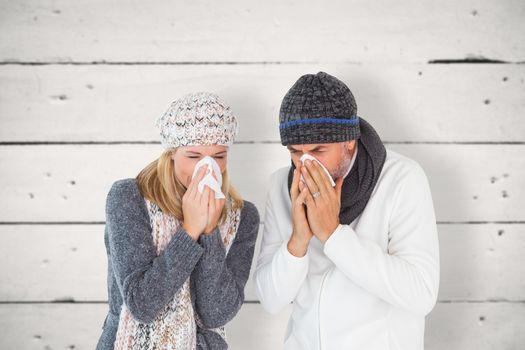 Sick couple in winter fashion sneezing against white wood