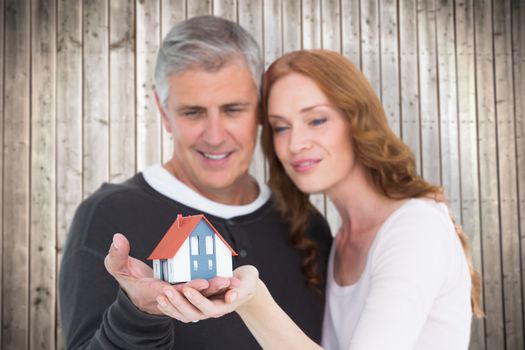 Casual couple holding small house against wooden planks background