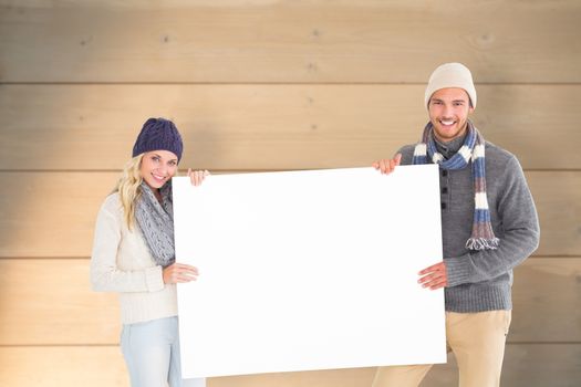 Attractive couple in winter fashion showing poster against bleached wooden planks background