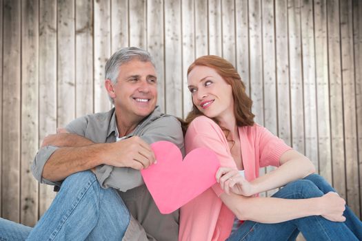 Casual couple holding pink heart against wooden planks background