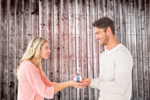 Attractive couple holding miniature house model against wooden planks