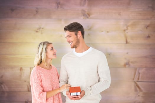 Attractive couple holding miniature house model against wooden planks