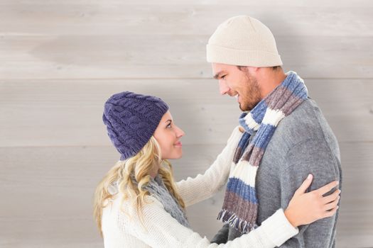 Attractive couple in winter fashion hugging against bleached wooden planks background