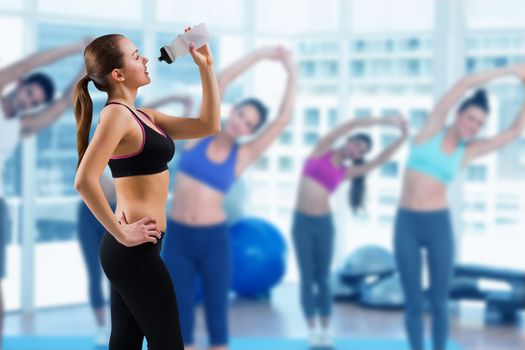 Composite image of fit brunette drinking from sports bottle