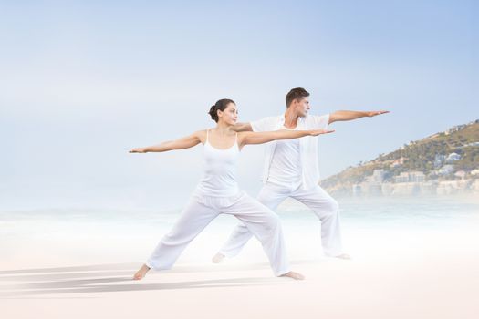 Peaceful couple in white doing yoga together in warrior position against beautiful beach and blue sky