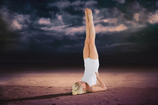 Fit young woman doing the shoulder stand pose against dark cloudy sky
