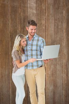 Attractive couple standing and using laptop against wooden planks background