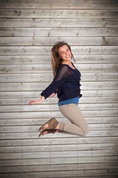 Full length of cheerful young woman jumping against wooden planks background