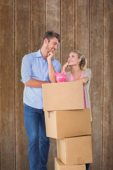 Attractive young couple leaning on boxes with piggy bank against wooden planks background