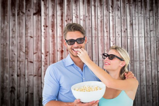 Happy young couple wearing 3d glasses eating popcorn against wooden planks