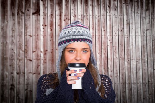 Beautiful woman in warm clothing drinking coffee against wooden planks