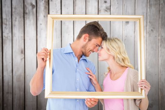 Attractive young couple holding picture frame against wooden planks