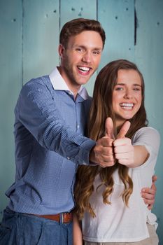 Happy couple gesturing thumbs up against painted blue wooden planks