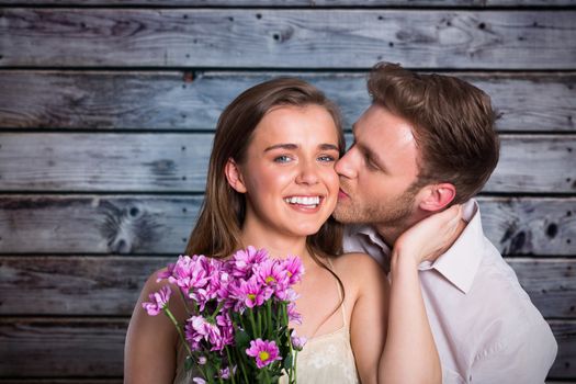 Man kissing woman as she holds flowers against grey wooden planks