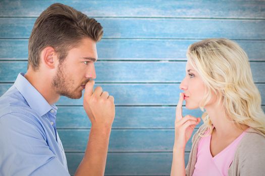 Young couple staying silent with fingers on lips against wooden planks