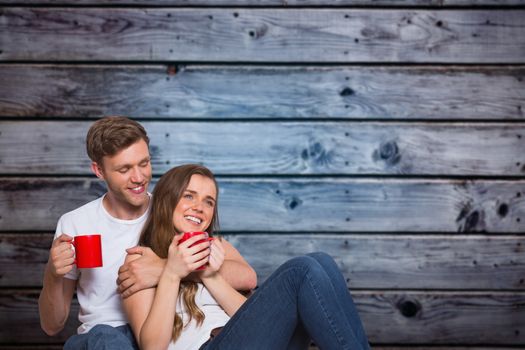 Couple with coffee cups sitting on floor against grey wooden planks