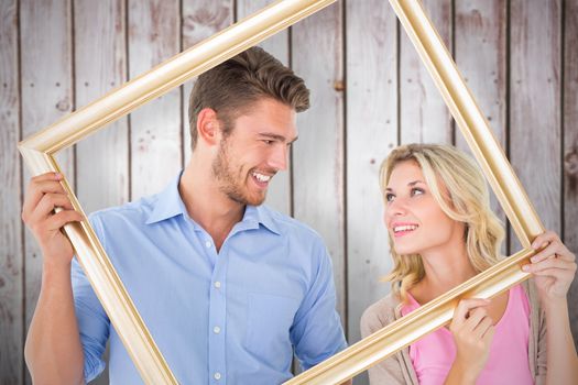 Attractive young couple holding picture frame against wooden planks