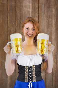 Oktoberfest girl holding jugs of beer against wooden planks background