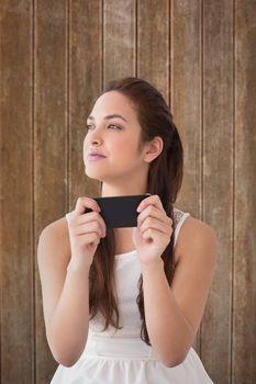 Thoughtful brunette holding her phone  against wooden planks background