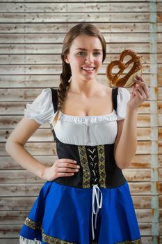 Pretty oktoberfest girl holding pretzel against faded pine wooden planks