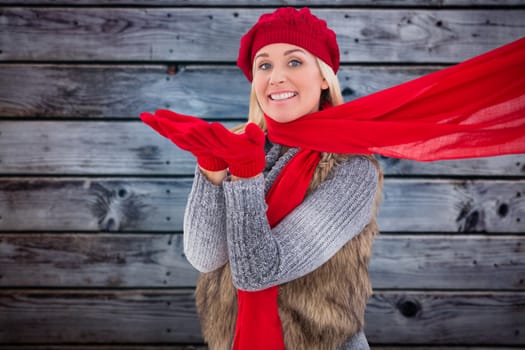 Blonde in winter clothes blowing kiss against grey wooden planks