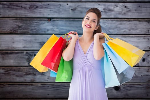 Thoughtful brunette holding shopping bags against grey wooden planks