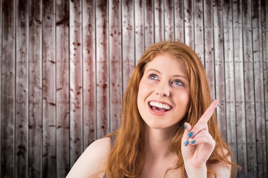 Pretty redhead pointing and looking up against wooden planks