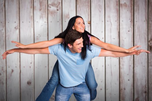 Young man giving girlfriend a piggyback ride against wooden planks