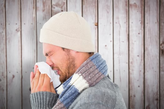 Handsome man in winter fashion blowing his nose against wooden planks