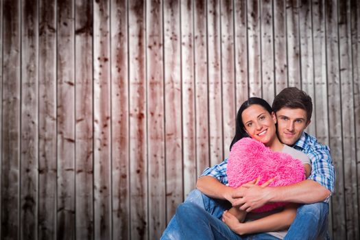 Young couple sitting on floor smiling against wooden planks