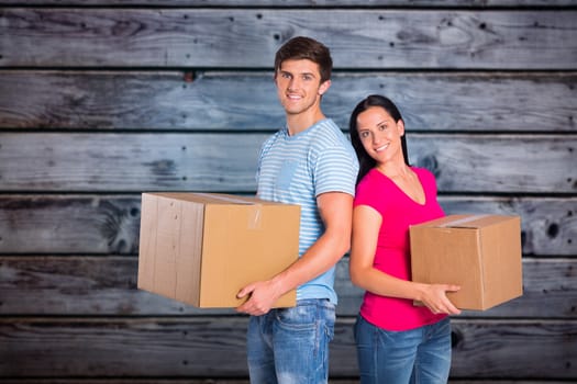 Young couple holding moving boxes against grey wooden planks