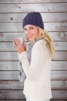 Pretty blonde in winter fashion holding mug against wooden planks
