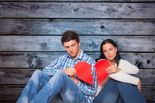Young couple sitting on floor with broken heart against grey wooden planks