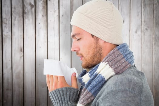 Handsome man in winter fashion blowing his nose against wooden planks