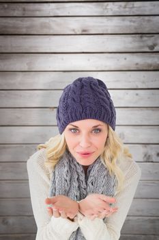 Pretty blonde in winter fashion blowing over hands against wooden planks