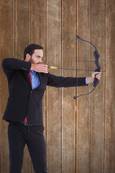 Focused businessman shooting a bow and arrow against wooden planks background