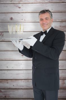 Smiling waiter holding tray with glasses with champagne against wooden planks