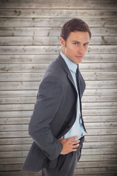 Serious businessman standing with hands on hips against wooden planks background